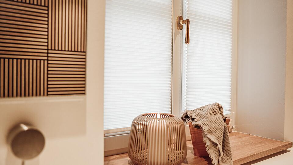 Weißes Wabenplissee am Fenster — strukturierter Stoff filtert sanft das Licht, gemütliche Fensterbank mit Kerzenhalter
