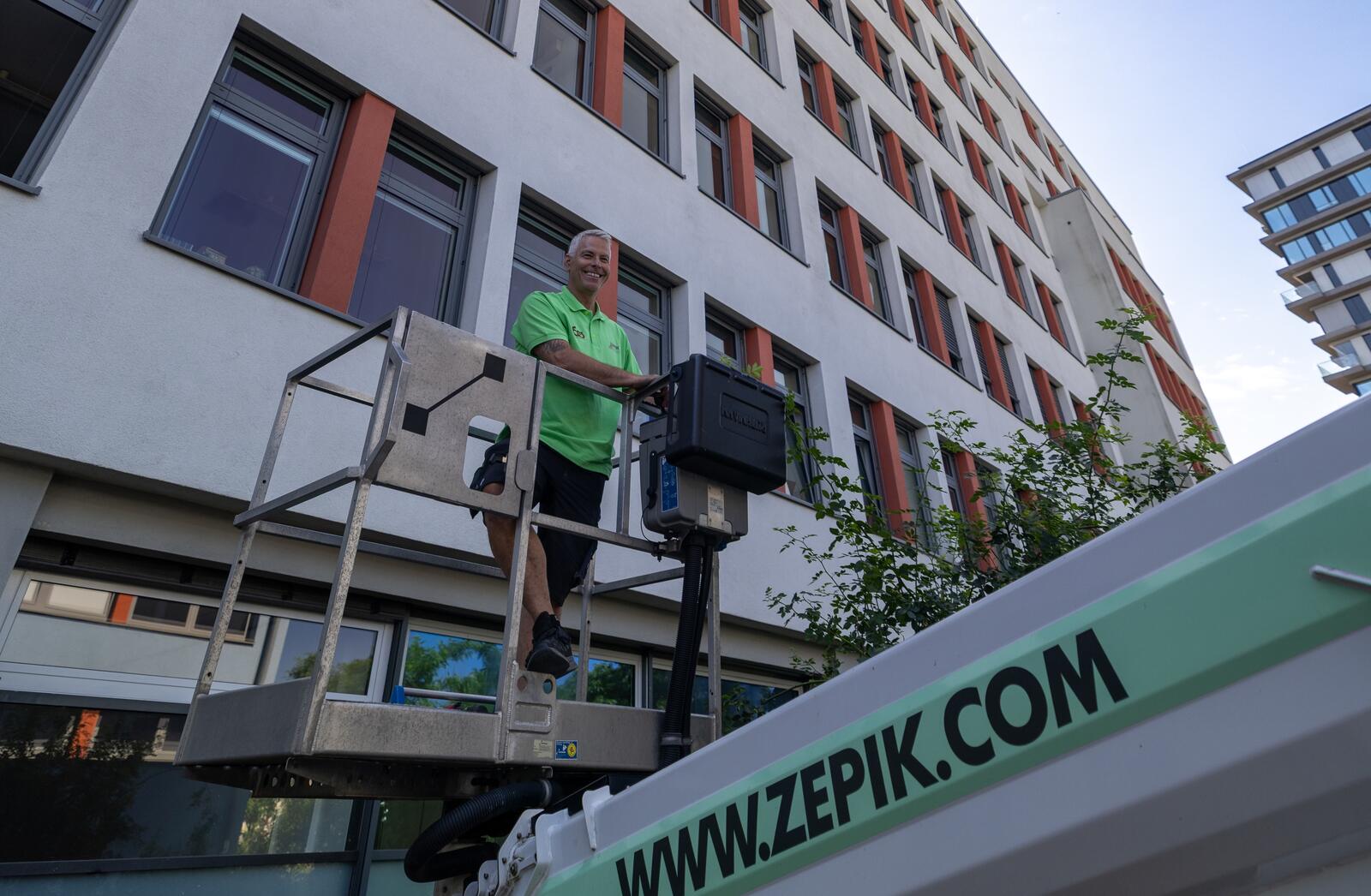 Zepik-Techniker steht lächelnd auf dem Steiger-LKW vor einem Berliner Bürogebäude — bereit zur Wartung