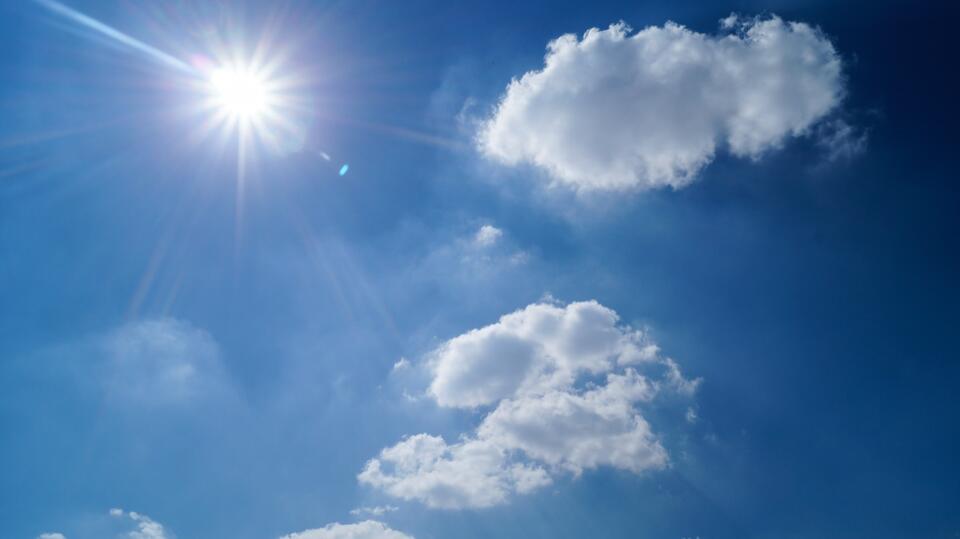 Strahlend blauer Himmel mit Sonne und Wolken
